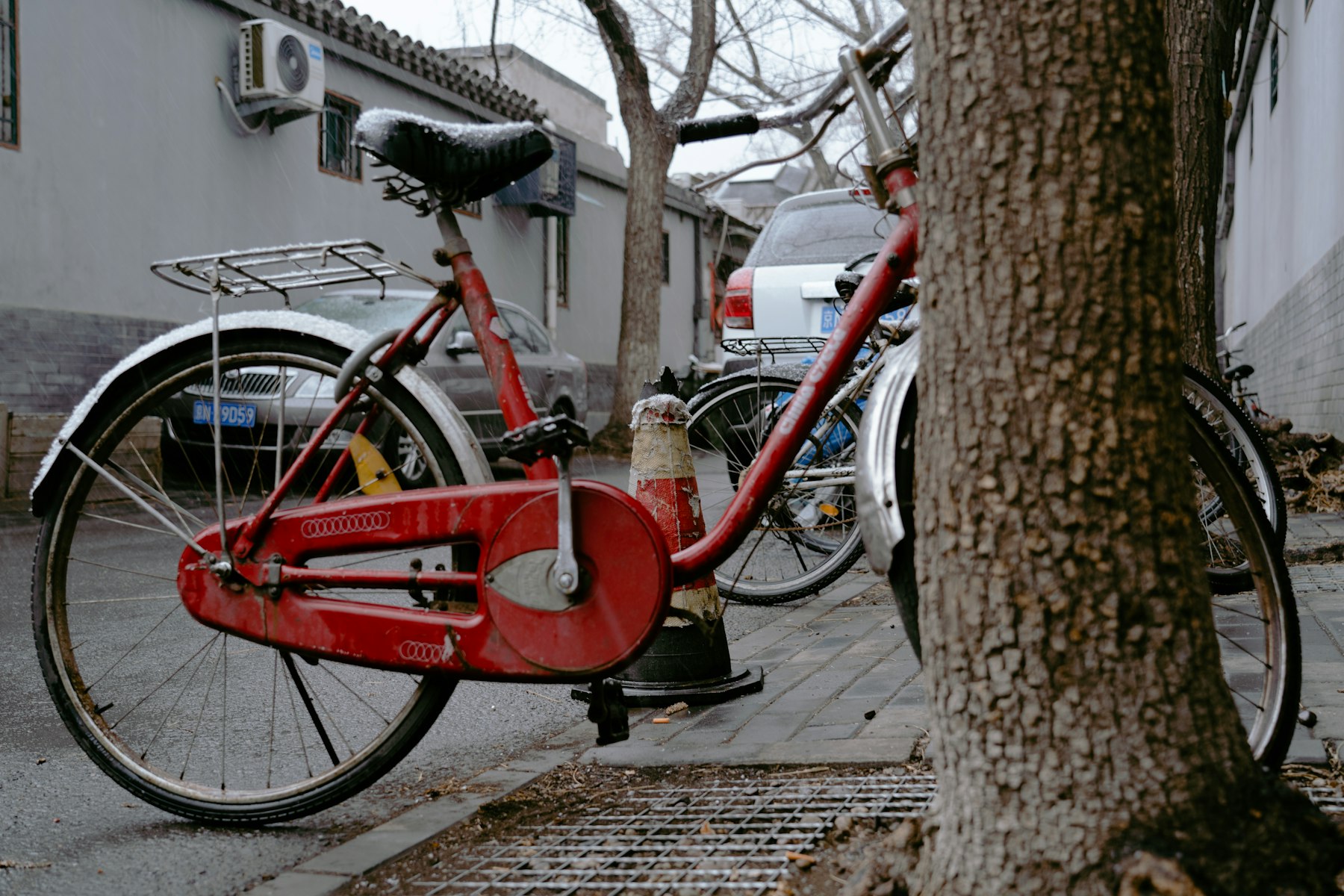 A red bicycle parked beside a tree in a residential Beijing hutong
